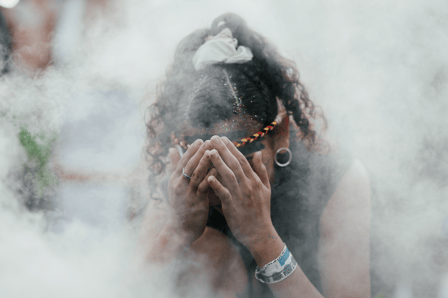 An Aboriginal woman in covers her face and crouches down in healing smoke.