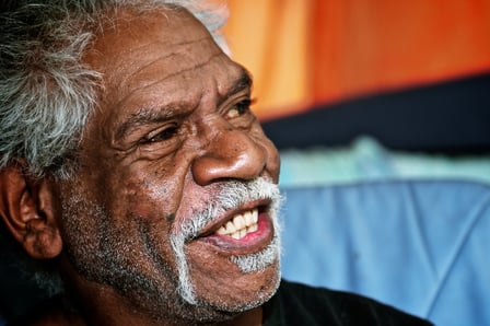 A close up of an Aboriginal man's face. He is in his 60s and smiling.