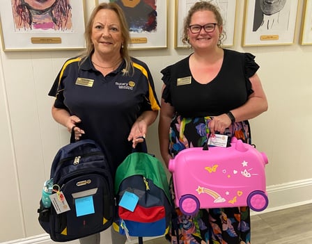 Two women from Rotary Club of Lismore smile holding suitcase donations for children in care.