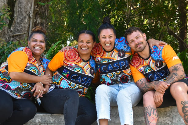 A group of smiling CASPA employees wearing shirts with Indigenous prints in an outdoor setting