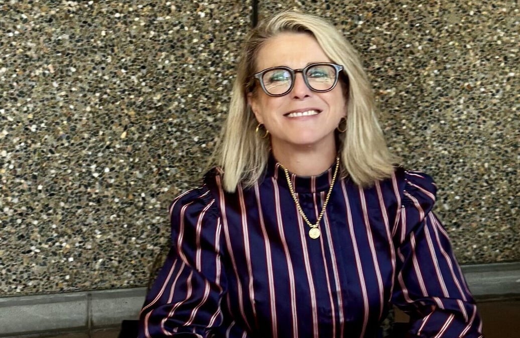 A smiling woman, dresses professionally, with blonde hair and glasses