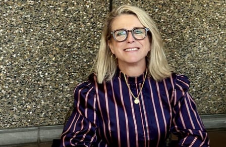 A smiling woman, dresses professionally, with blonde hair and glasses