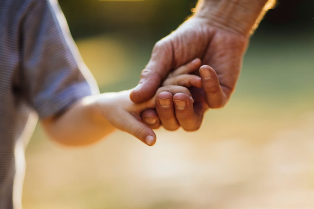 An adult gently holds the hand of a child.