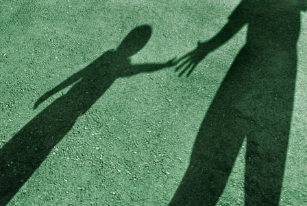 Shadows of a child and adult reach for each others hands on a green background