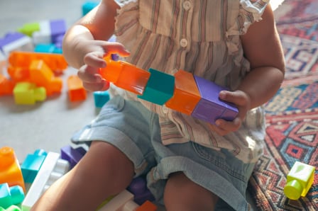 A child with pale skin plays with brightly coloured blocks in a home setting