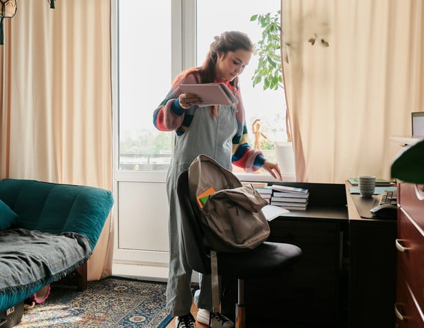 A teenage girl stands in a comfortable living area placing books into a backpack