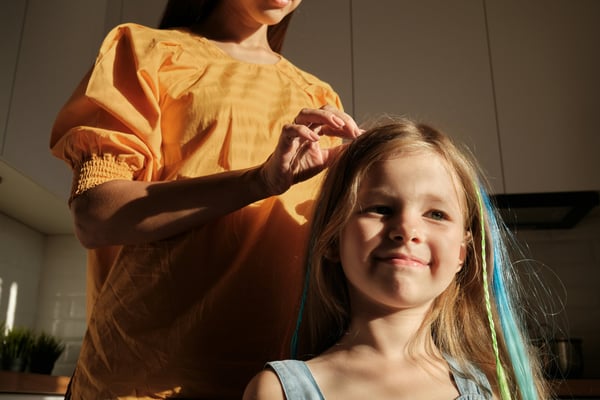 An adult does a smiling white child's hair in a warm, home setting