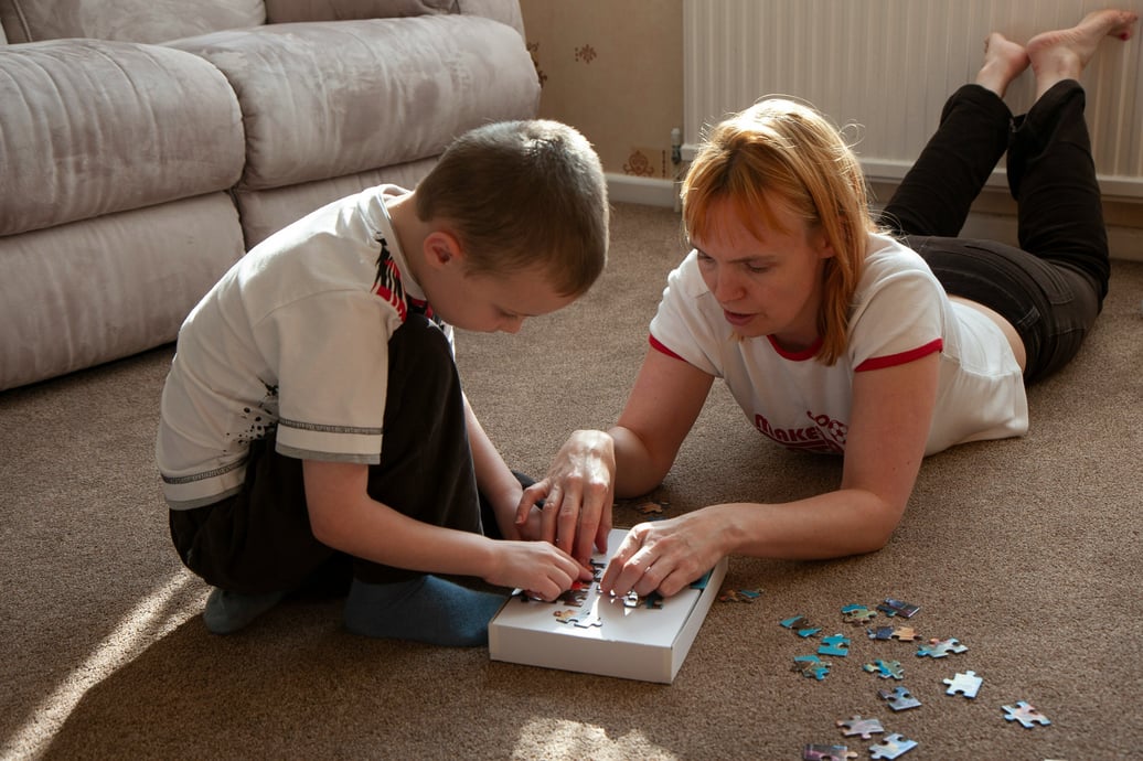 A woman and young person work on a puzzle together on the floor in a living room setting