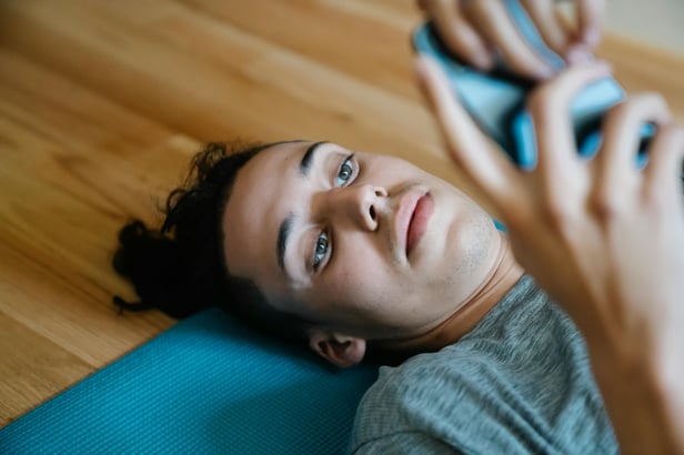 Young light skinned person lying on the ground looking at their smartphone. Their expression is neutral.